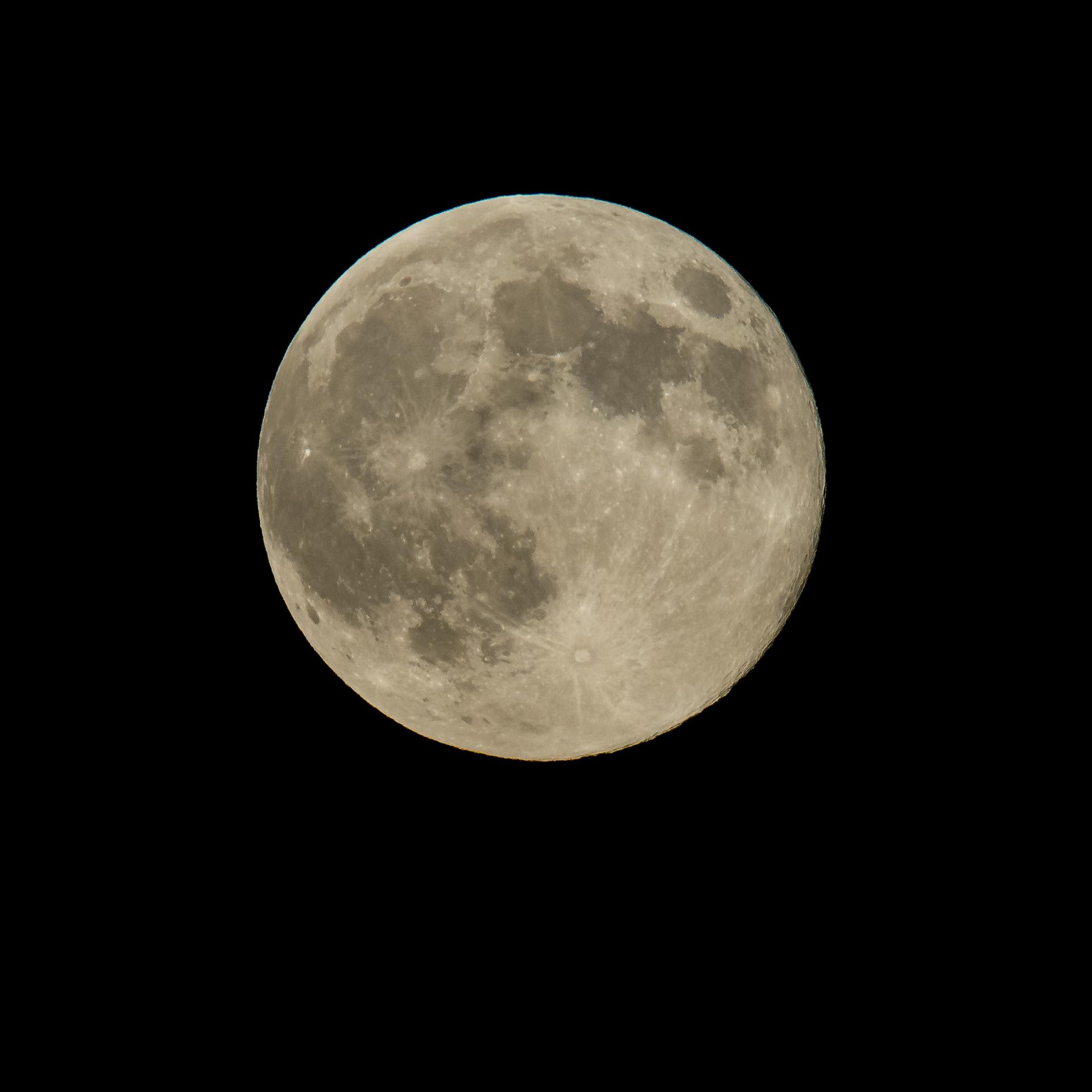 La Luna llena, sola y centrada sobre un cielo completamente negro, con las manchas oscuras de sus mares repartidas por la mitad superior y un cráter brillante en la parte de abajo del que salen rayas claras hacia los bordes.