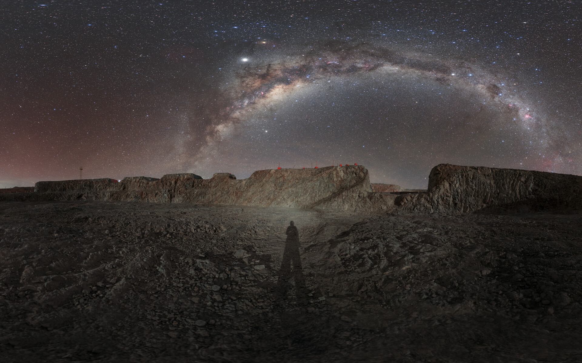 Panorámica nocturna del cerro Armazones, en Chile: el arco de la Vía Láctea cruza el cielo sobre la explanada donde se construye el telescopio ELT, con la silueta a contraluz de una persona en primer plano.