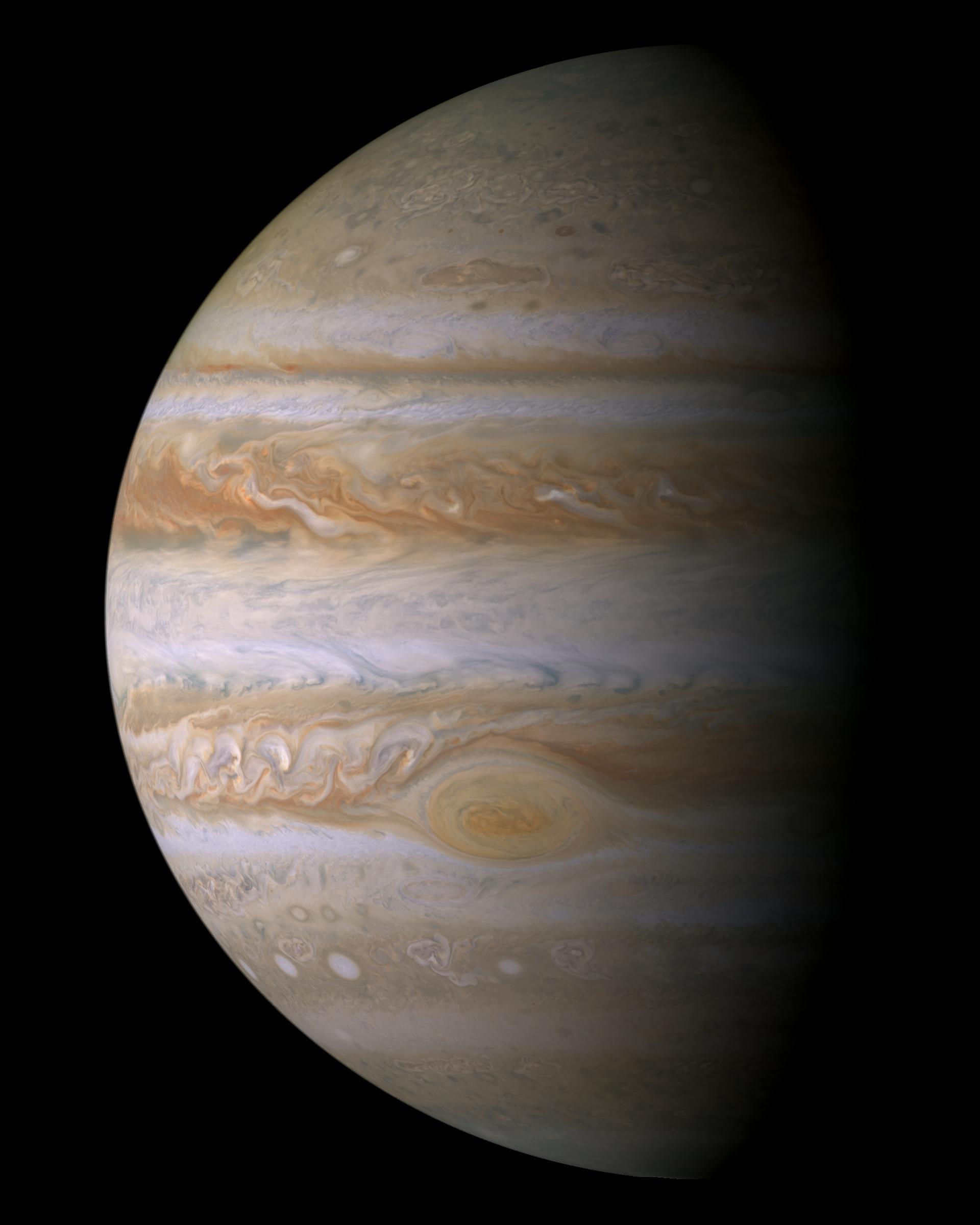 El disco de Júpiter fotografiado por la sonda Cassini, con el borde derecho en sombra: bandas horizontales de nubes en tonos crema, ocre y anaranjado, la Gran Mancha Roja como un óvalo pálido en la mitad inferior y varios óvalos blancos más pequeños en la banda de debajo.
