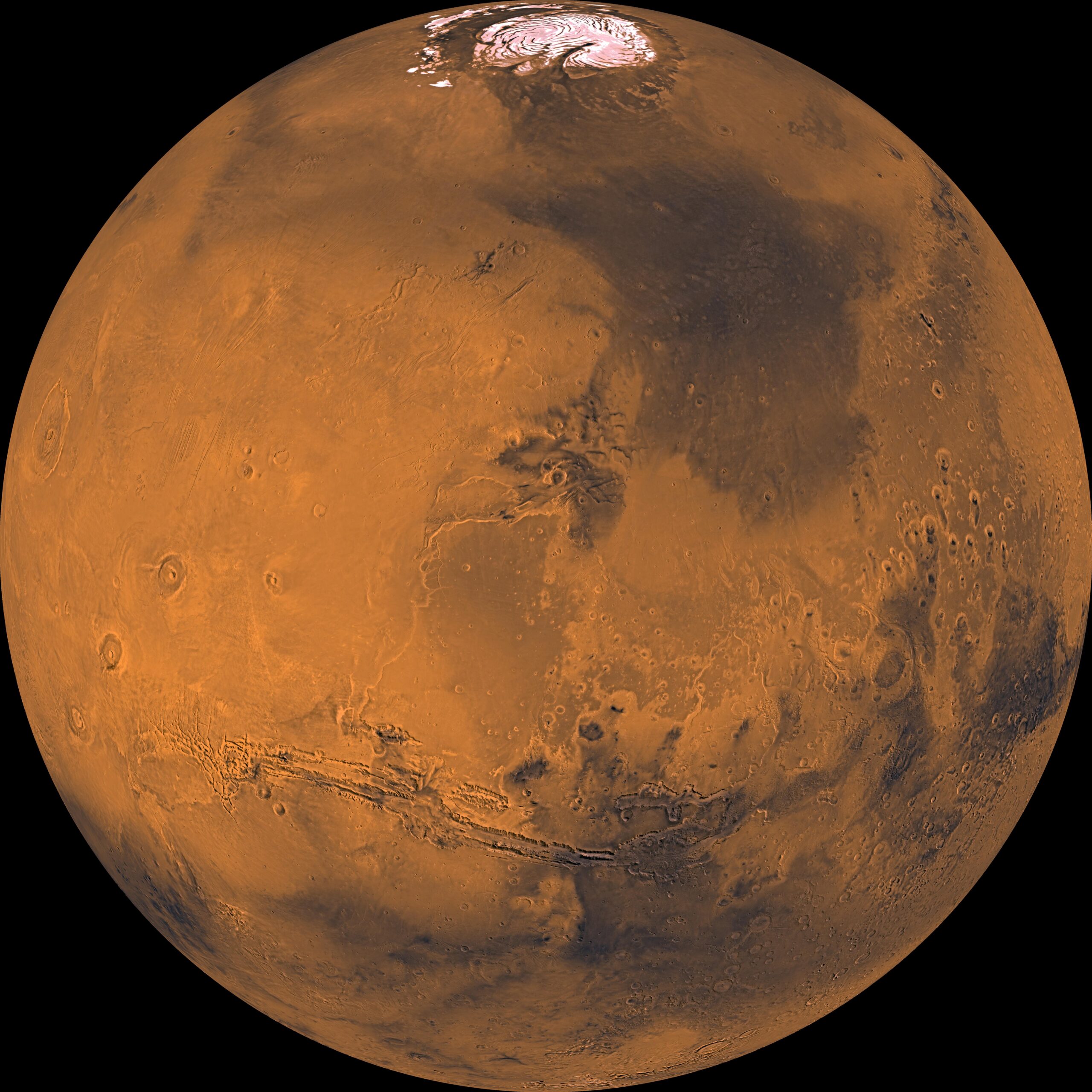 El globo de Marte en un mosaico de las sondas Viking: una esfera de tonos ocres y anaranjados, con el casquete polar norte blanco en la parte de arriba, el largo sistema de cañones de Valles Marineris cruzando por debajo del centro y los grandes volcanes de la región de Tharsis a la izquierda.