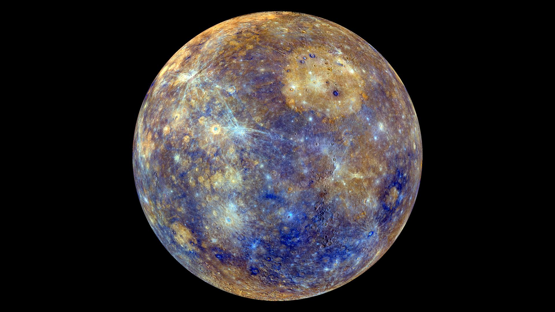 El globo completo de Mercurio sobre fondo negro, en color realzado: el disco aparece moteado de azules y ocres, cubierto de cráteres, con rayas blanquecinas que salen de los impactos más recientes y una gran mancha circular color arena arriba a la derecha.
