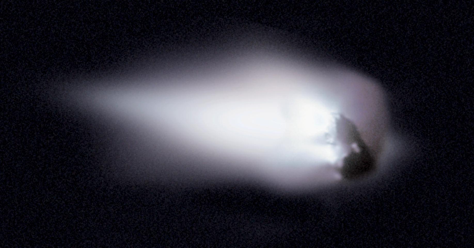 Sobre un fondo negro, un cuerpo oscuro e irregular ocupa la parte derecha de la imagen y de él brotan hacia la izquierda dos chorros de polvo blanco muy brillantes que se ensanchan hasta formar una nube difusa.