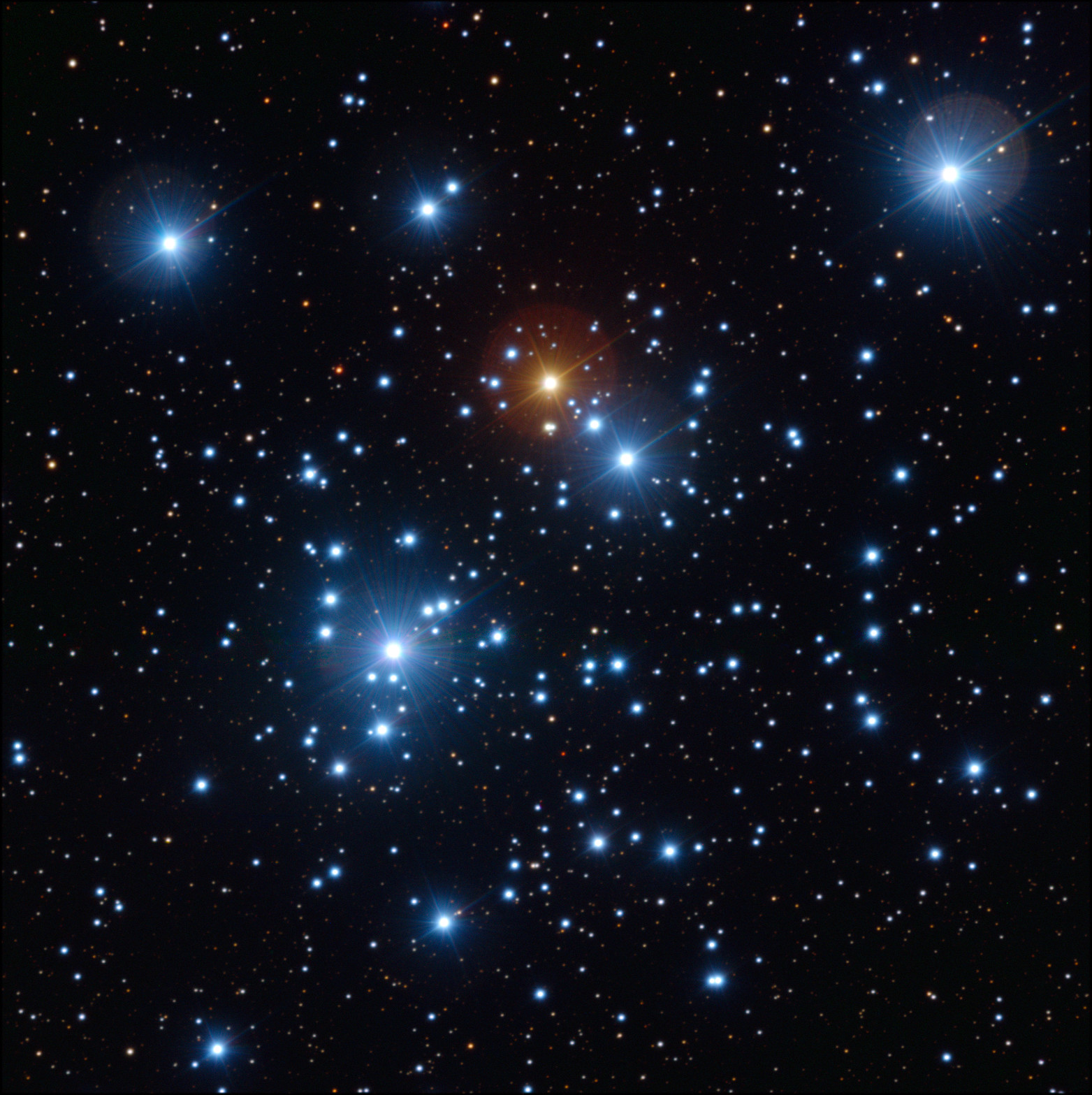 Cúmulo estelar del Joyero sobre fondo negro: decenas de estrellas de un blanco azulado intenso, varias con destellos en forma de cruz, y en el centro superior una sola estrella brillante de color naranja, rodeada de un halo rojizo.